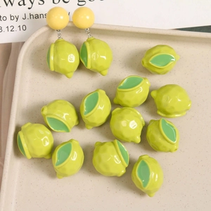 Macro detail of yellow resin lemon charms and DIY earrings on a beige speckled tray