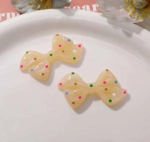 Close-up of cream resin bow charms with colorful polka dots on a white ceramic plate