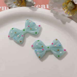 Close-up of light blue resin bow charms with colorful polka dots for DIY jewelry