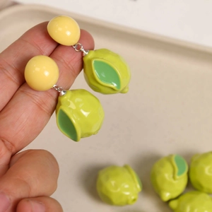 Macro shot of 3D resin lemon earrings with green leaves held by hand for DIY jewelry