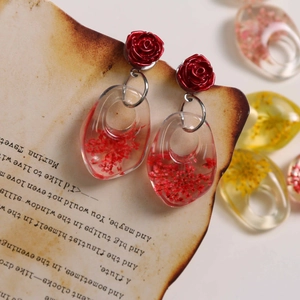 Detail of resin earrings with red roses and dried flowers on vintage paper background
