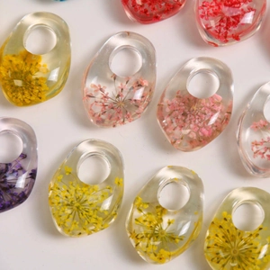 Detailed view of handmade resin oval pendants with real dried flowers for DIY jewelry