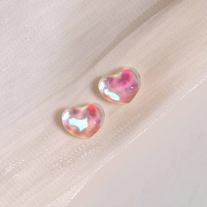 Detailed view of iridescent heart-shaped resin charms on a cream silk textured background