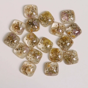 Macro detail of square resin charms with real dried flowers and gold beads for DIY jewelry