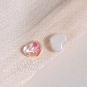 Macro shot of iridescent and pearl white heart-shaped charms on champagne silk fabric