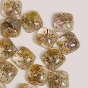 Flat lay of square resin beads with dried flowers and gold accents for DIY jewelry