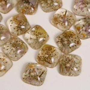 Macro shot of square resin cabochons with dried flowers and gold beads for DIY jewelry