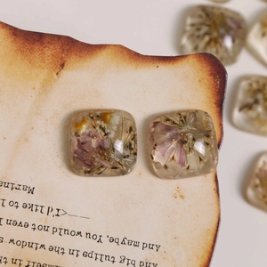 Detailed macro of handmade clear resin earrings with purple dried flowers and gold beads