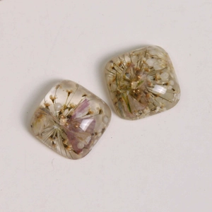 Macro detail of square resin charms with dried flowers and gold beads for jewelry making