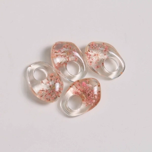 Macro shot of four asymmetric resin charms with embedded pink dried flowers for DIY jewelry