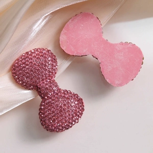 Detail of pink rhinestone-encrusted bow-shaped DIY charms on elegant satin background