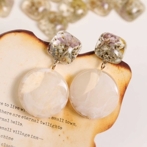 Detail of vintage resin earrings with dried flowers and marble pattern on old newspaper