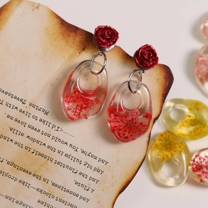 Detail of clear resin earring pendant with red dried flowers and rose top on vintage paper