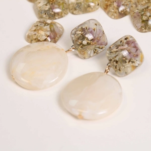 Close-up of handmade resin earrings with real purple dried flowers and marble effect drops