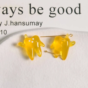 Close-up of translucent amber resin tooth pendants with gold pins on a white ceramic tray