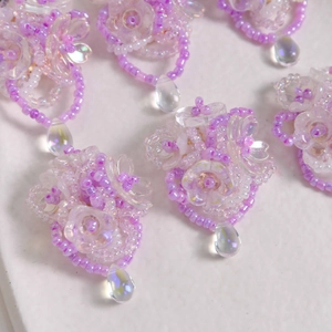 Macro detail of handmade iridescent purple beaded flower earring accessory with teardrop charm