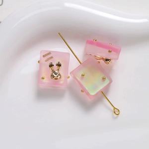 Detailed macro view of a pink resin rectangular bead with a golden rabbit inlay for DIY