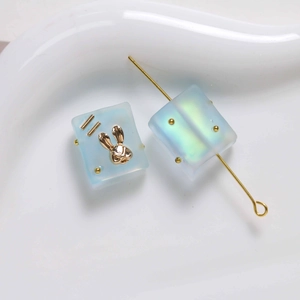 Macro detail of frosted blue resin square beads with gold rabbit and aurora shimmer