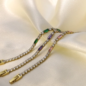 Detalle de tres pulseras tenis chapadas en oro con piedras de colores sobre tela de seda