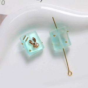 Macro detail of blue translucent resin square bead with golden rabbit relief and T-pin