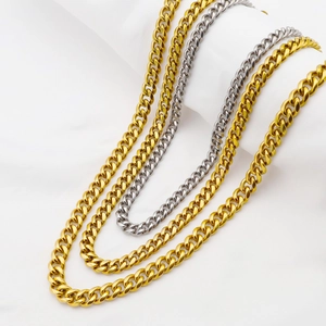 Détail des chaînes à mailles cubaines dorées et argentées sur fond de tissu blanc