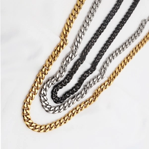 Détail de colliers à grosses mailles cubaines en or, argent et noir sur tissu blanc plissé