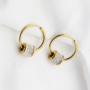Close-up of golden hoop earrings with pavé-set zircon beads on a soft fabric background