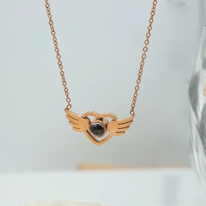 Macro shot of rose gold heart and wings pendant necklace with a center projection stone
