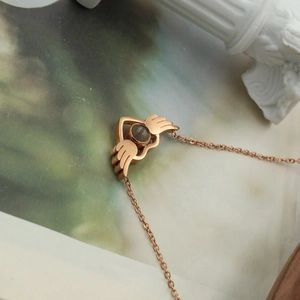 Detail of rose gold heart and wings pendant necklace featuring a central projection stone