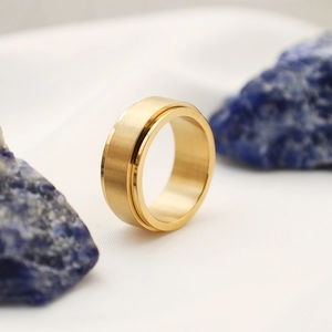 Dettaglio macro dell'anello rotante in titanio spazzolato oro su tessuto strutturato e pietre