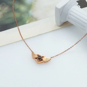 Rose gold angel wing heart pendant necklace on a white surface with roman column decor
