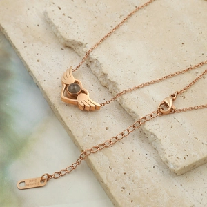Rose gold angel wings heart necklace with projection stone on beige textured stone