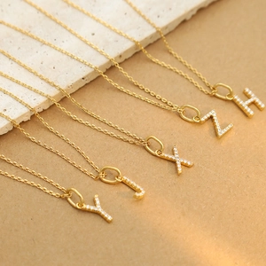 Detail showing various gold letter pendants with micro-set rhinestones on fine chains