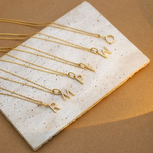 Gold stainless steel initial necklaces with sparkling crystals on a textured beige stone