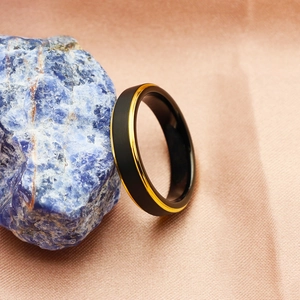 Detail of matte black and gold tungsten ring on a textured blue stone with soft background