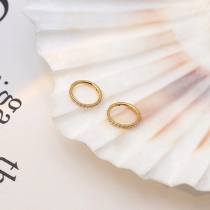 Anneau de nez doré élégant avec zircons blancs présenté dans un coquillage blanc