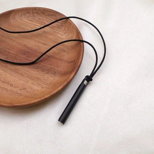 Collar de silbato negro mate con cordón sobre fondo textil blanco con luz suave