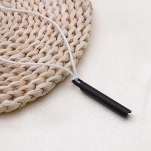 Primer plano de un colgante de silbato negro mate con cordón blanco sobre fondo texturizado