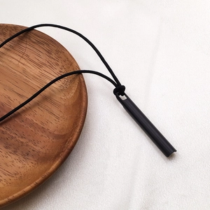 Collar de silbato minimalista en metal negro mate con cordón sobre fondo de tela blanca