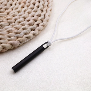 Collar colgante de silbato negro mate minimalista con cordón blanco sobre un tapete de tela