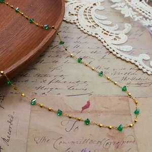 Collier en or avec cristaux verts sur fond de papier manuscrit ancien et dentelle