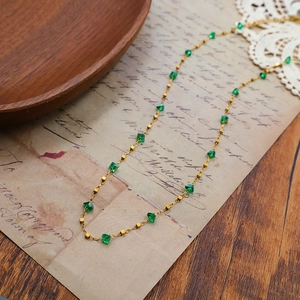 Collier doré élégant orné de pierres vert émeraude facettées sur fond de papier vintage