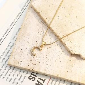 Detail einer goldenen Halskette mit C-Anhänger und kleinen weißen Perlen auf Steinplatte