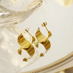 Boucles d'oreilles créoles larges en acier doré poli sur un plateau miroir chic