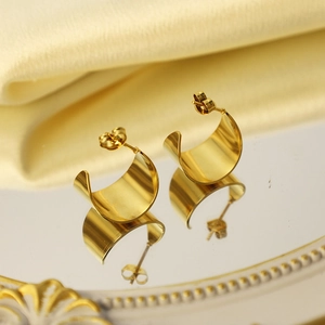 Détail des boucles d'oreilles larges en C en acier doré sur un plateau miroir élégant