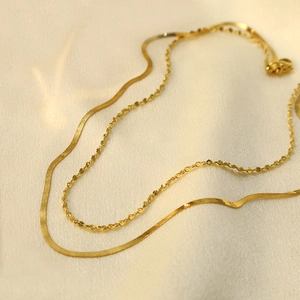 Dettaglio di una collana dorata a doppio strato con catena piatta a serpente e testurizzata