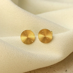 Makroaufnahme goldener fächerförmiger Ohrstecker mit Sonnenstrahl-Textur auf Stoff