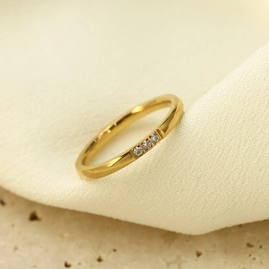 Detail eines goldenen Titanrings mit drei eingelegten Zirkonia auf Steinhintergrund