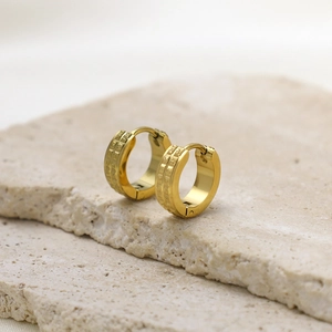 Detailed view of gold hoop earrings with textured square relief pattern on stone base