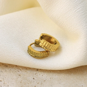 Detailopname van gouden oorringen met geribbelde textuur op een elegante neutrale stof
